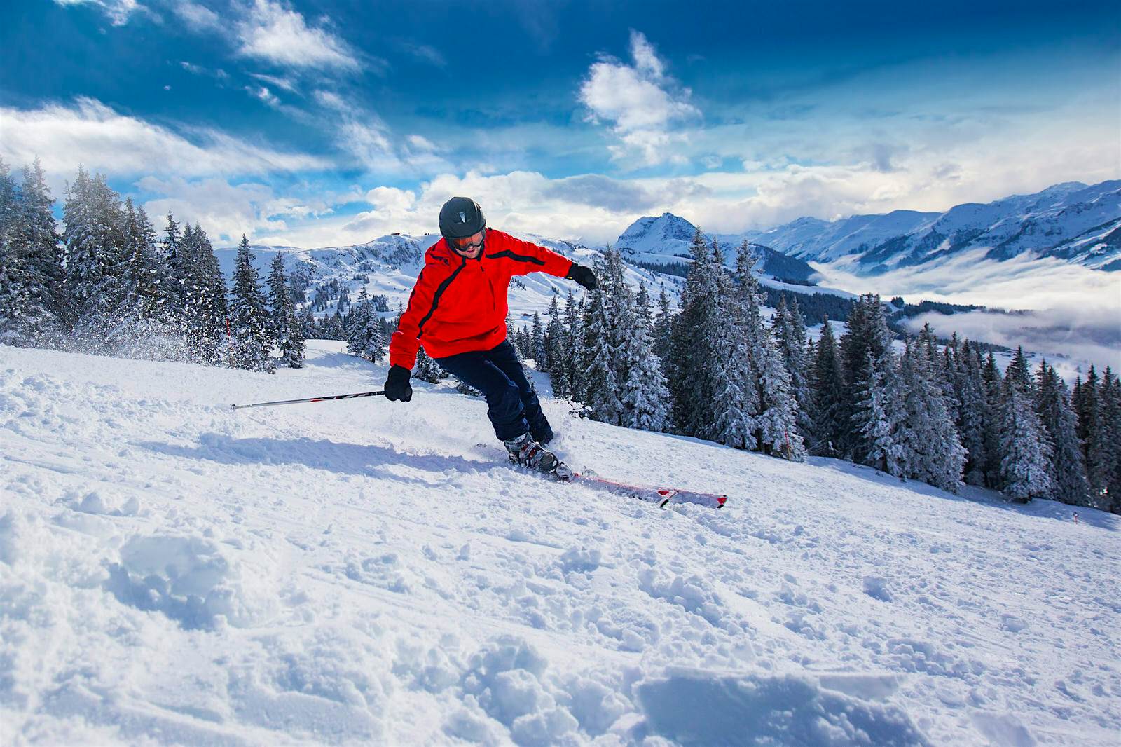 Austrian ski slope Person in full ski gear skiing down a snowy slope. The blue sky and Alpine mountains are in the background