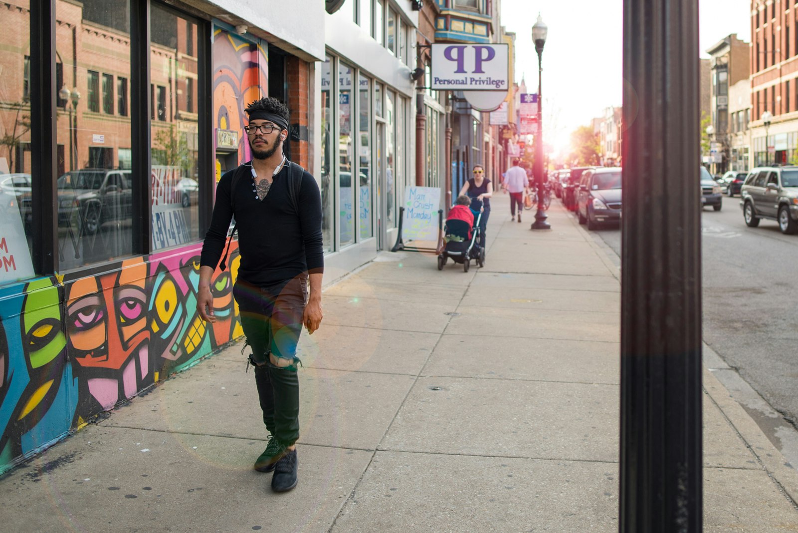 young man walks along a neighborhood street past a colorful shop facade as the sun sets