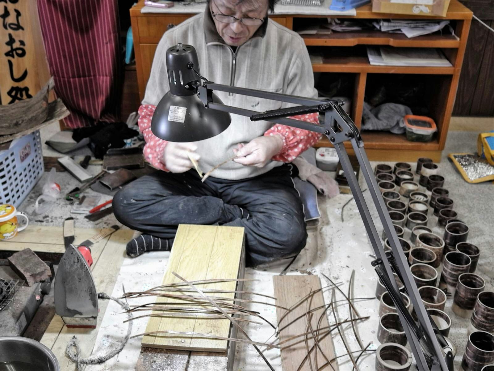 A woodworker sits on the floor of his studio working with strips of cherry bark © Manami Okazaki / Lonely Planet
