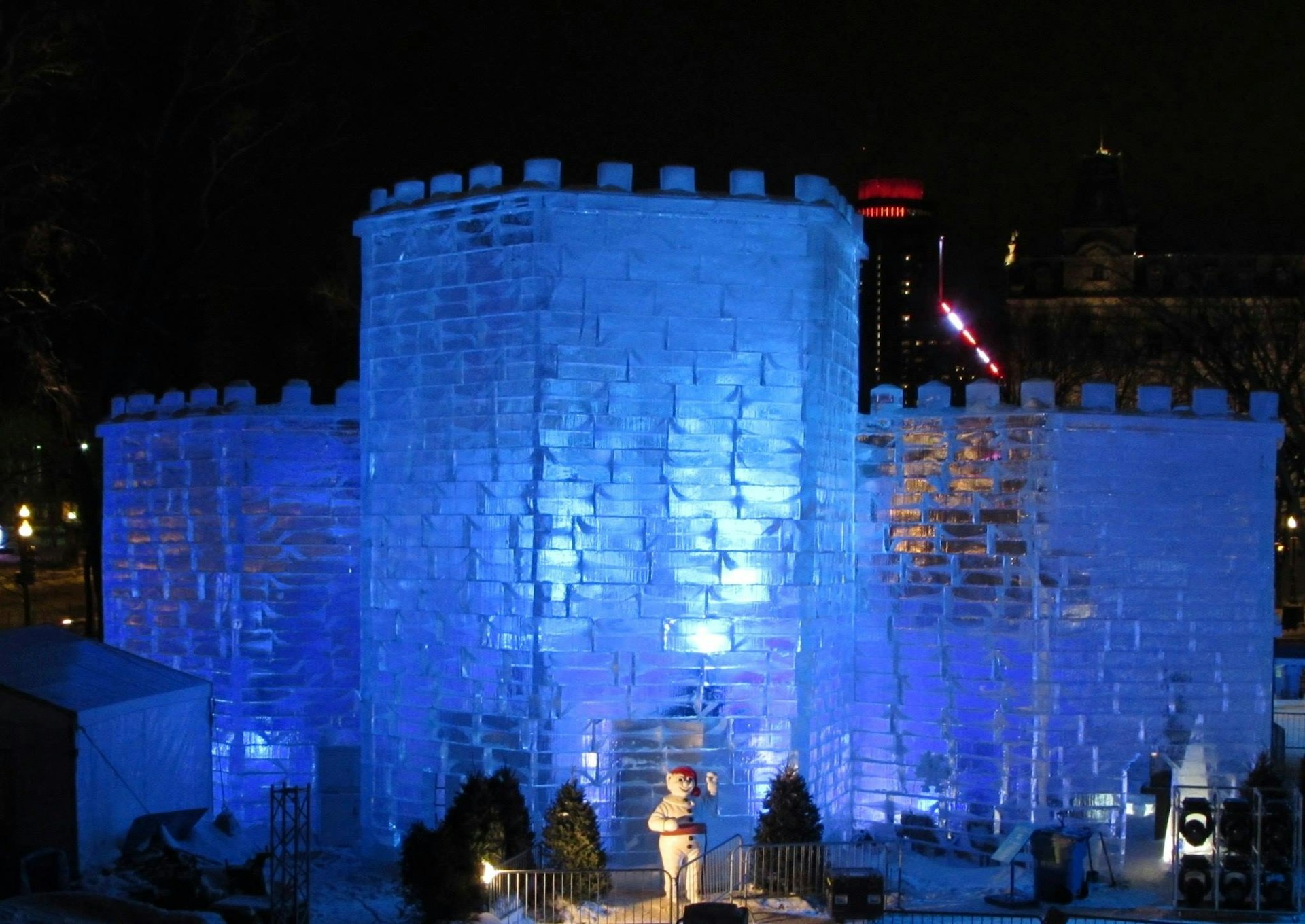 A transparent castle made of giant ice blocks is lit with a blue light from inside, against a pitch black sky in Québec City.
