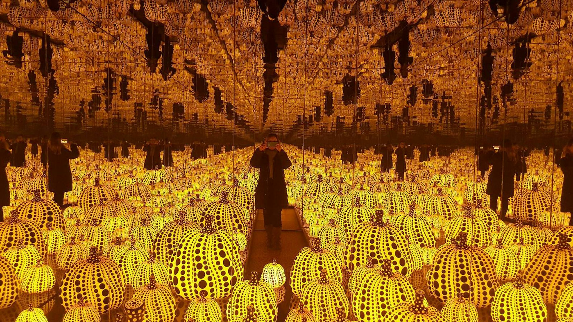 The writer stands amongst a mirrored room of orange-lit pumpkin sculptures in the Chiostro del Bramante
