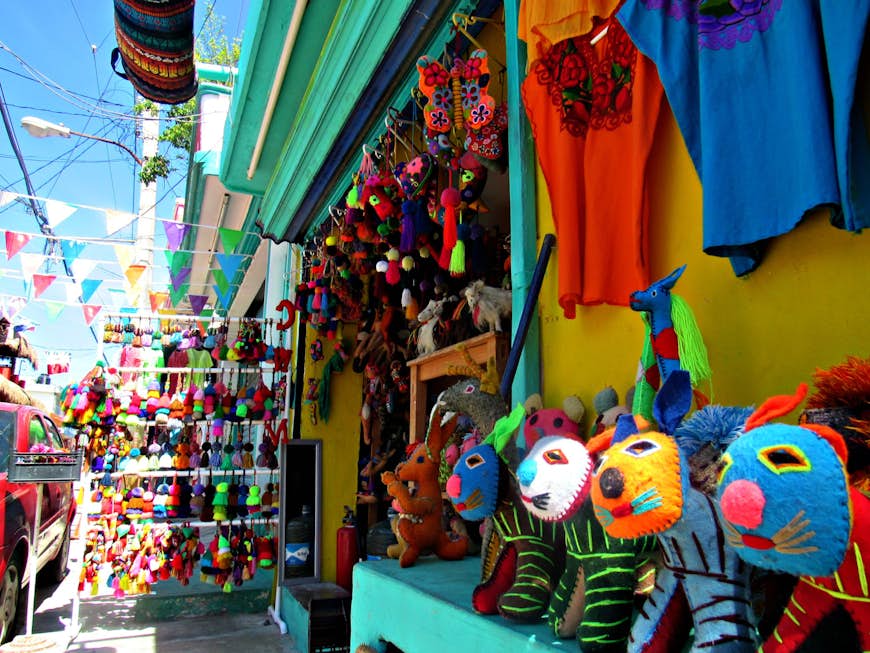 En butik full av färgglada mexikanska hantverk är öppen mot gatan © Laura Winfree / Lonely Planet