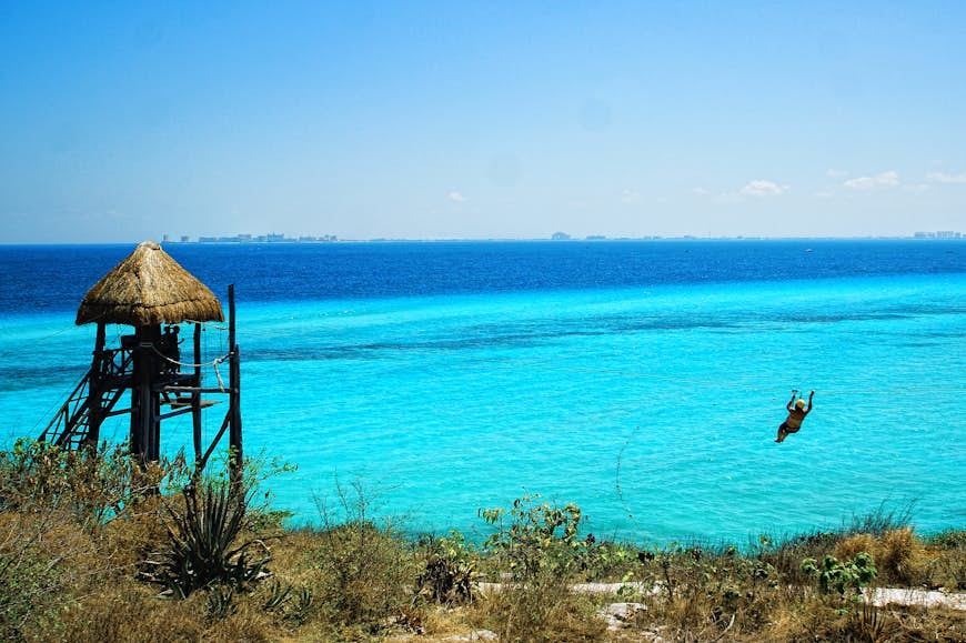 En person ziplines över Karibiska havet på Isla Mujeres med Cancún i bakgrunden © Infinite Highway / Getty Images