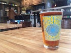An amber-coloured beer in a pint glass with Jaws brewery branding on a wood table © Megan Eaves / Lonely Planet