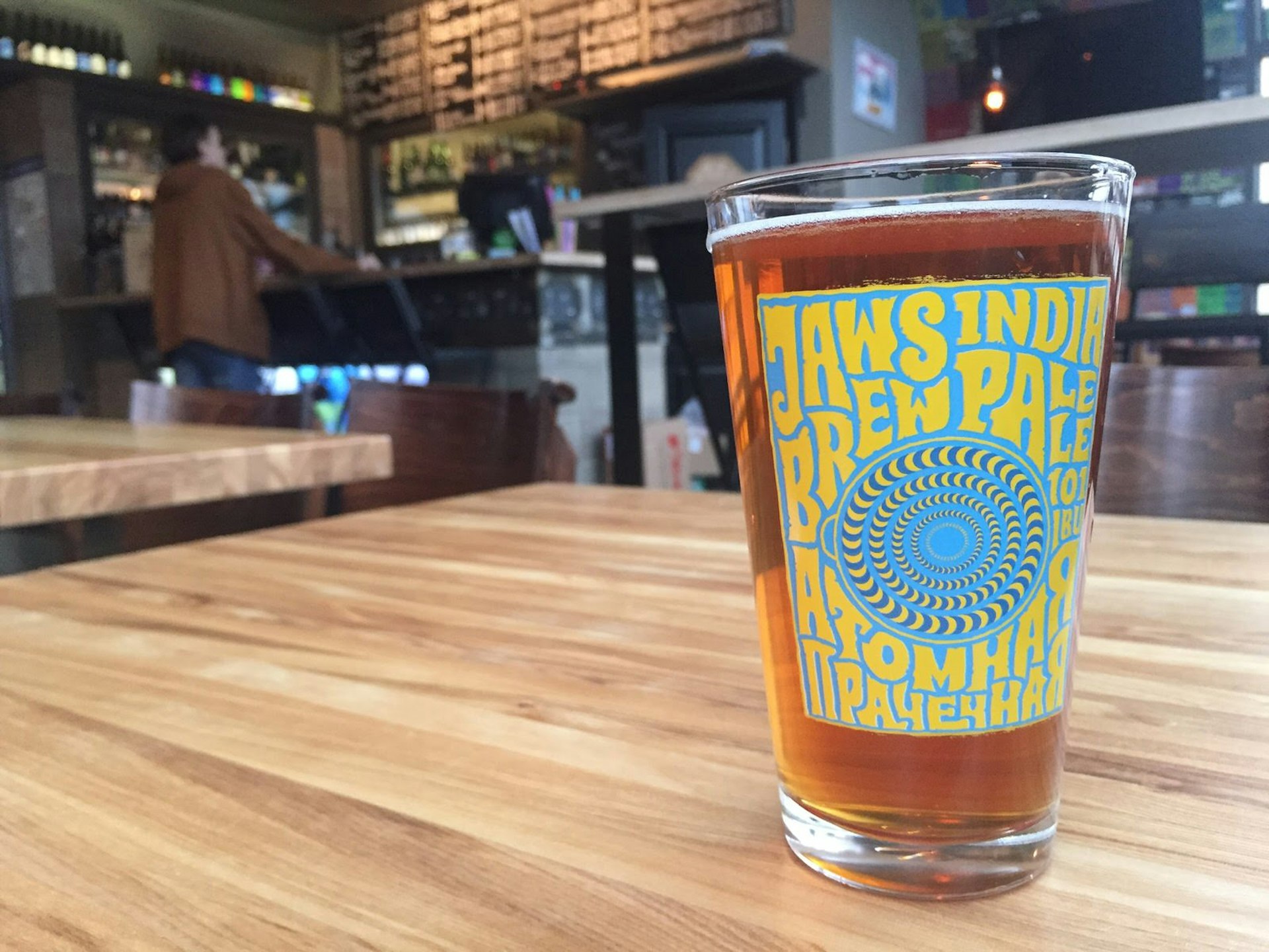 An amber-coloured beer in a pint glass with Jaws brewery branding on a wood table © Megan Eaves / Lonely Planet