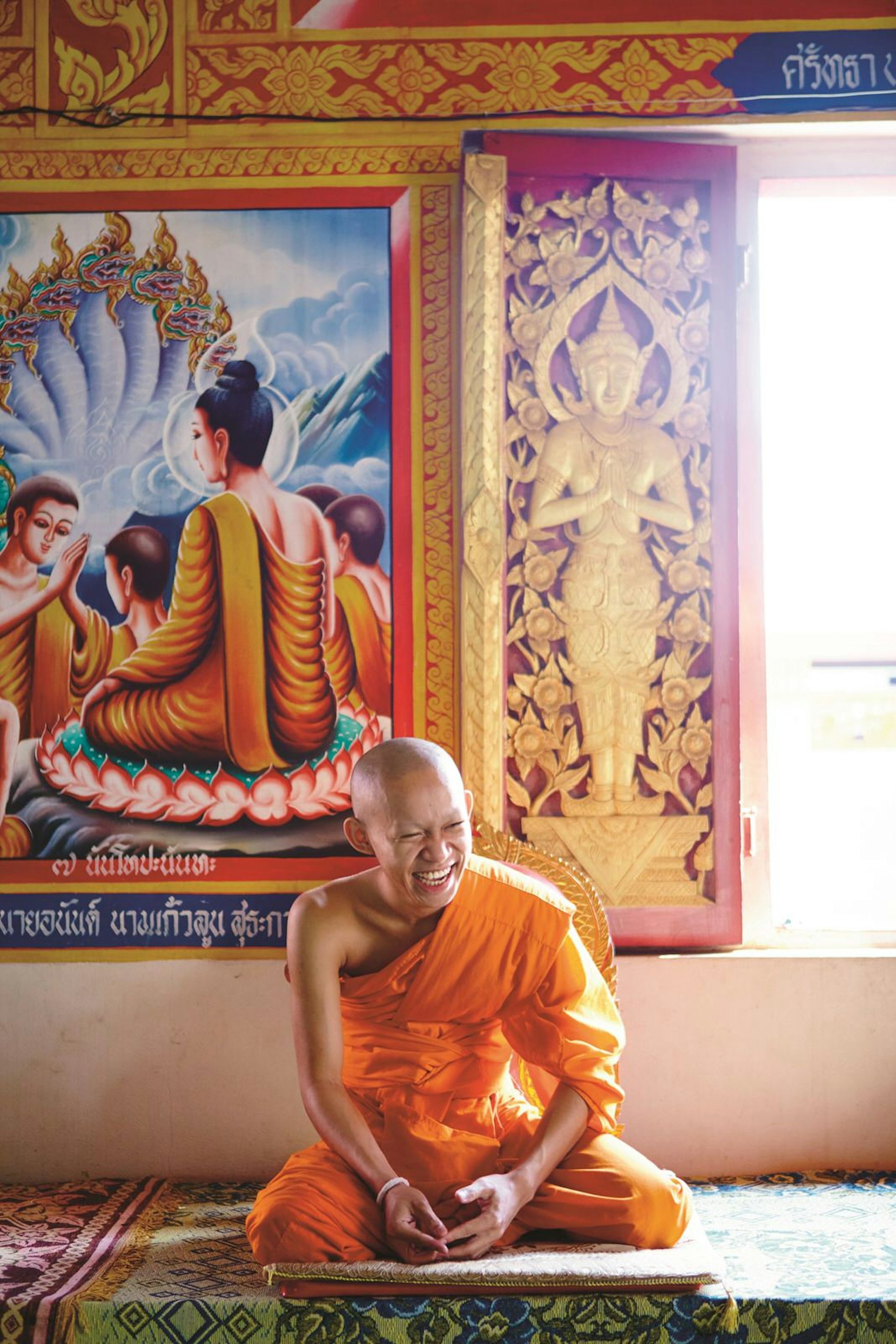 A monk smiles while sitting beneath a Buddha mural © Matt Munro / Lonely Planet