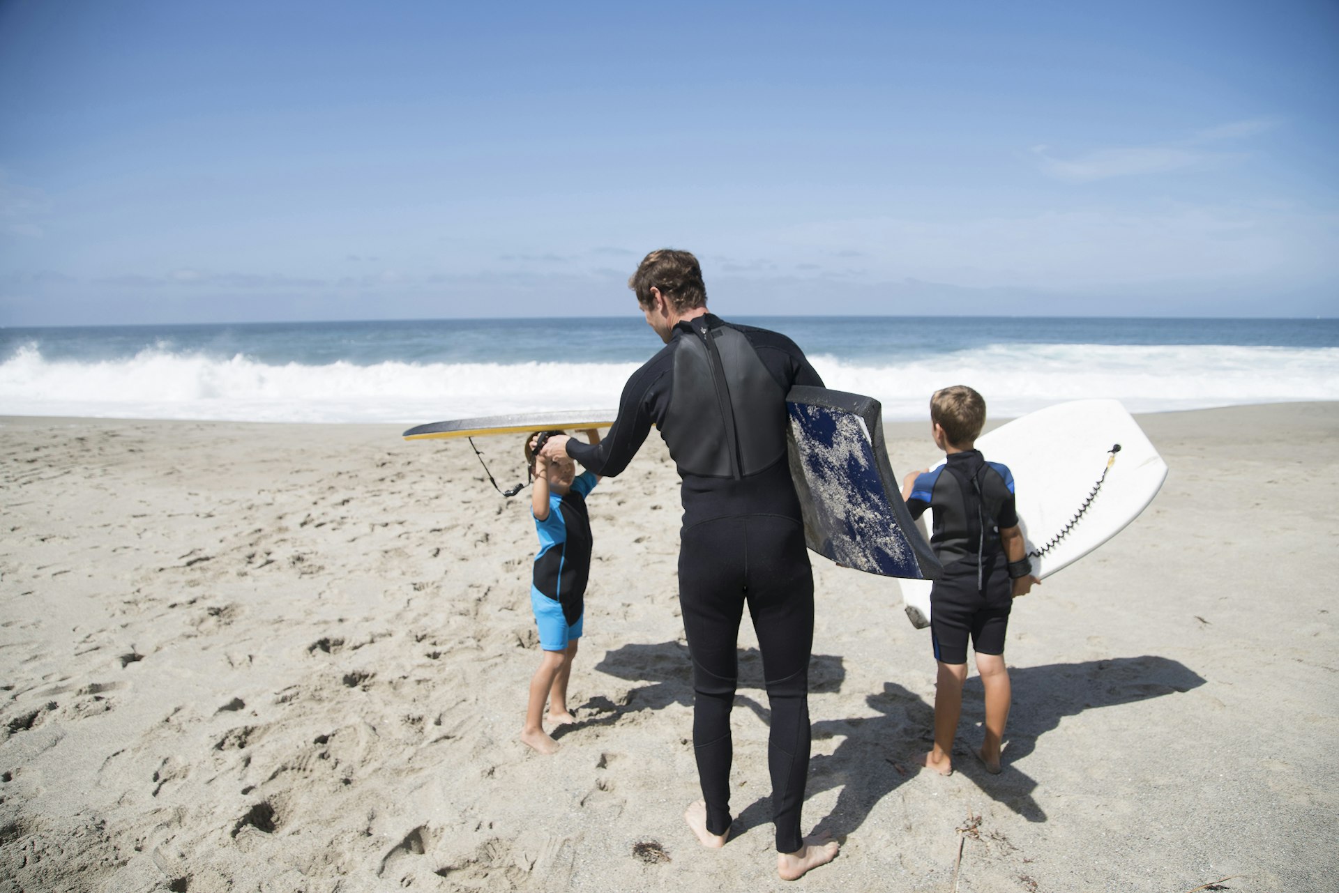 Features - Rear view of father and two sons preparing to go bodyboarding on beach, Laguna Beach, California, USA