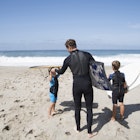 Features - Rear view of father and two sons preparing to go bodyboarding on beach, Laguna Beach, California, USA