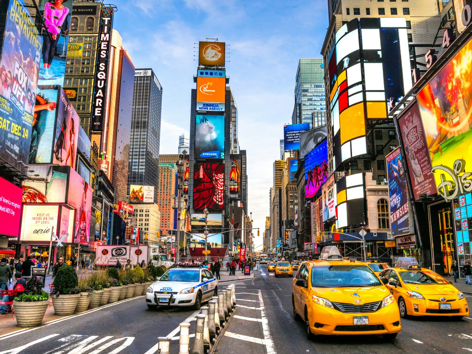 A colourful New York street scene with neon signs and bright yellow taxis in the foreground