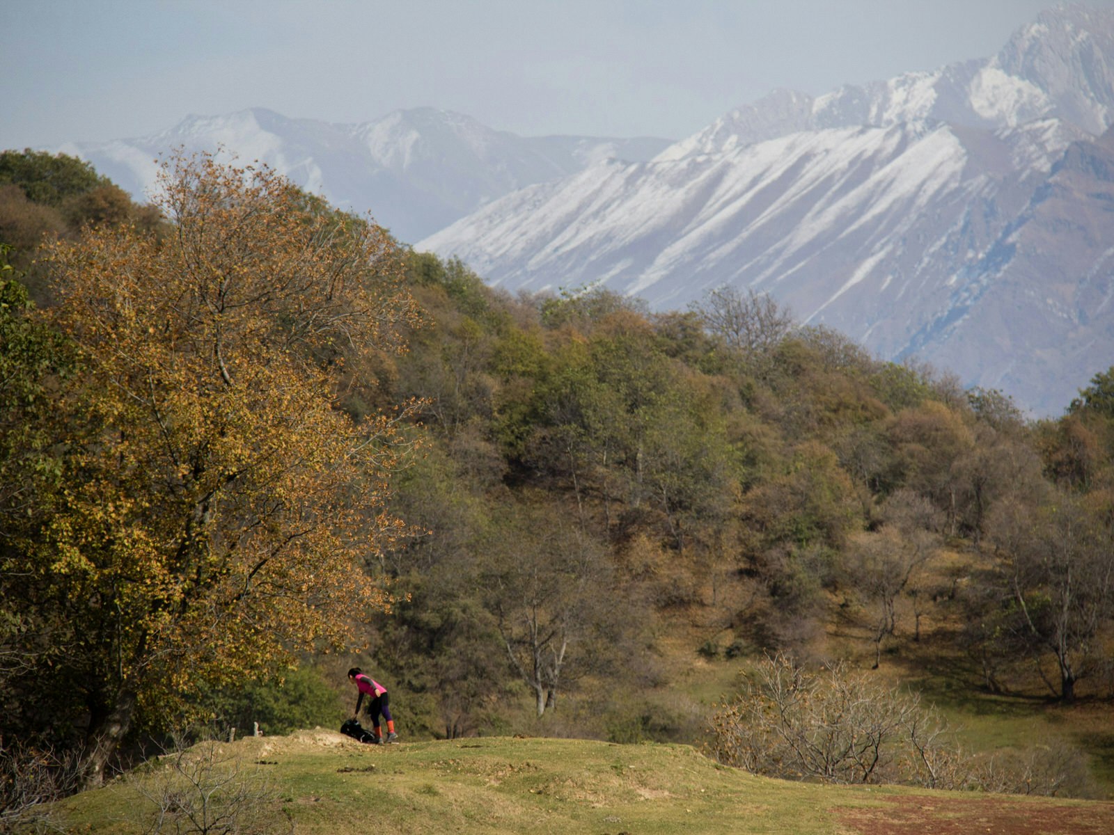 A tourist rests on a hilltop above the forests of Arslanbob with the mountains of the Babash-Ata ridge in the background © Stephen Lioy / Lonely Planet
