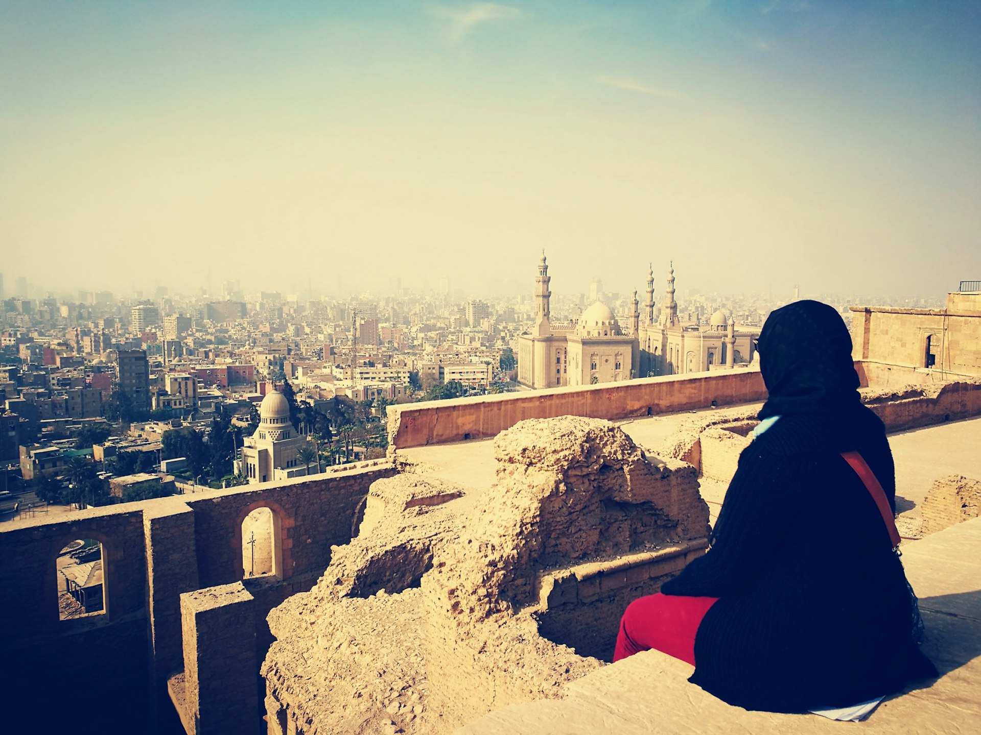 A woman in hijab sits over looking the city of Cairo, Egypt. Image by Ahmed Mandoub / EyeEm / Getty Images