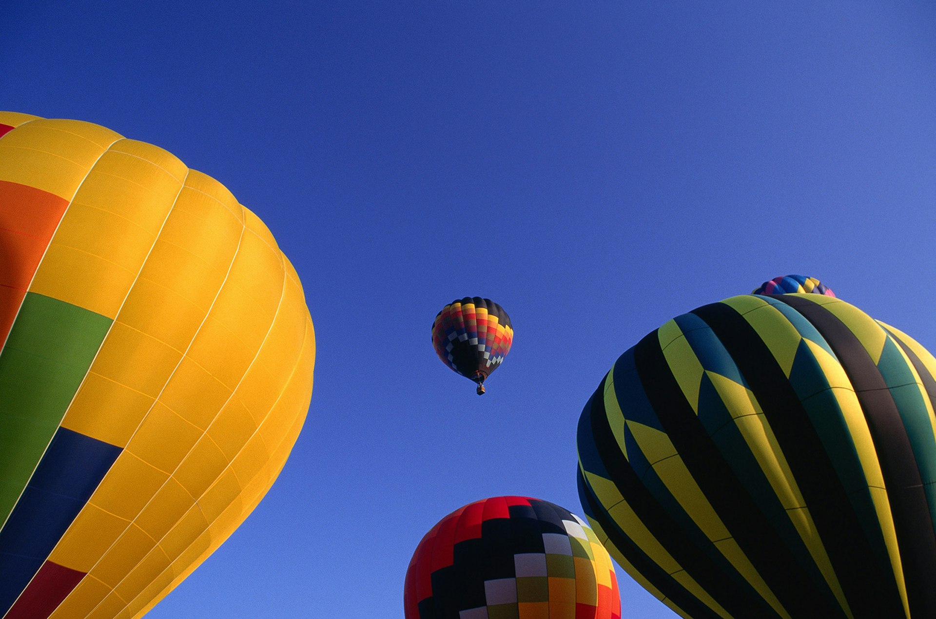 close-up of three hot air balloons with a fourth in the distance, in a clear blue sky