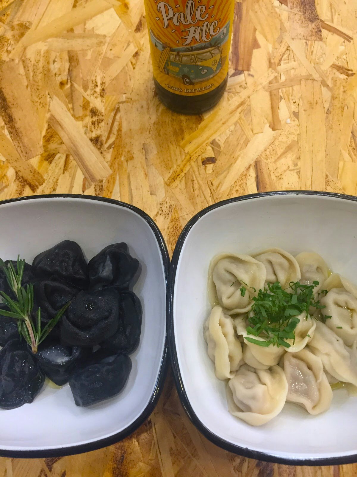 A plate of dark dumplings and a plate of light dumplings on a wooden table with a bottle of craft beer at Lepim i Varim in Moscow © Megan Eaves / Lonely Planet