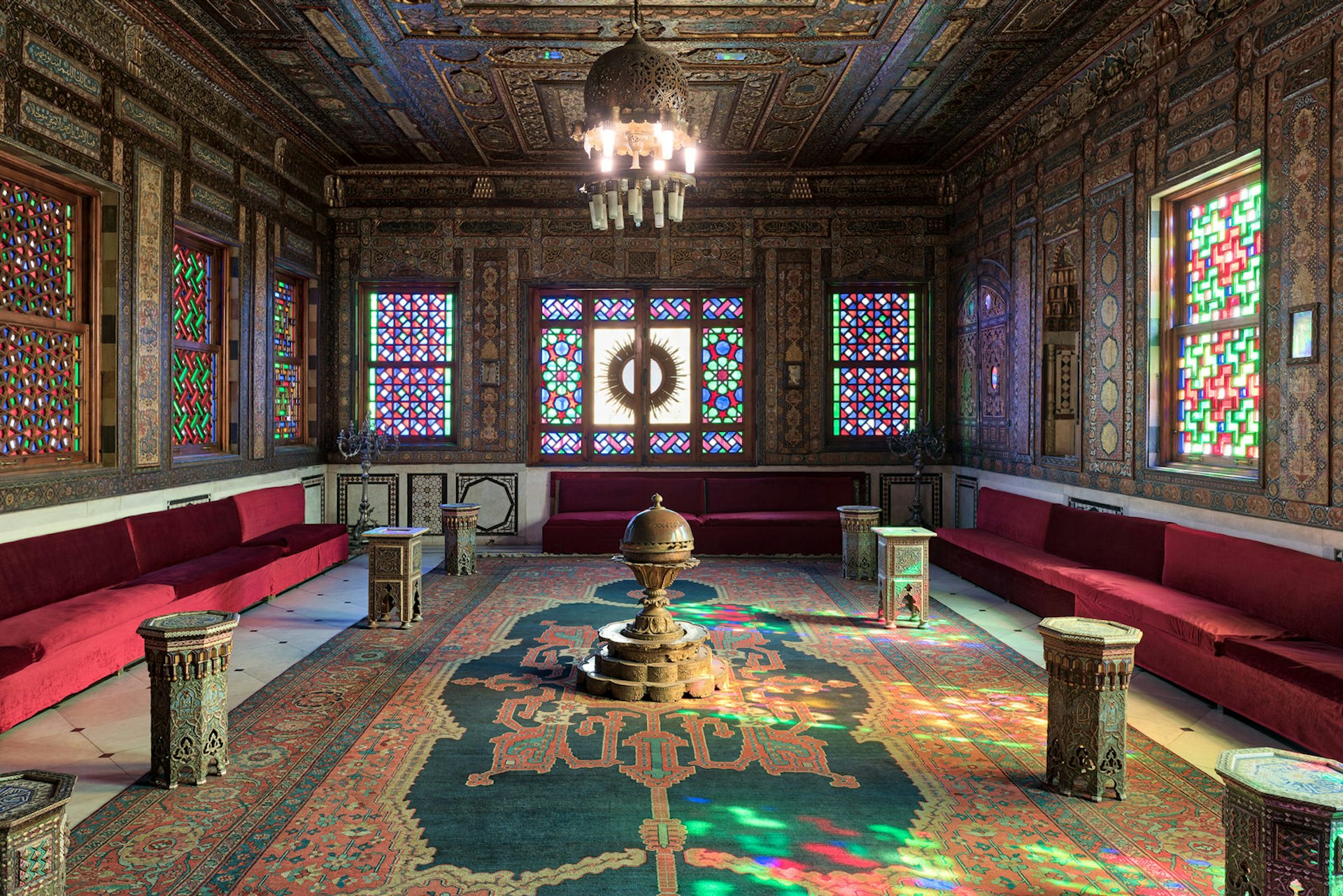 Manial Palace of Prince Mohammed Ali in Cairo, Egypt. Syrian Hall with ornate wooden wall and ceiling, windows with coloured stained glass and Ottoman Empire logo, old ornate chandelier. Image by Khaled El Adawy / Shutterstock