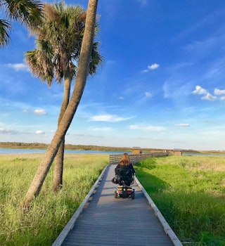 wheelchair user rolls down a wooden birdwalk over seagrass in Florida