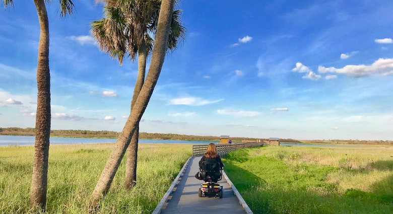 wheelchair user rolls down a wooden birdwalk over seagrass in Florida