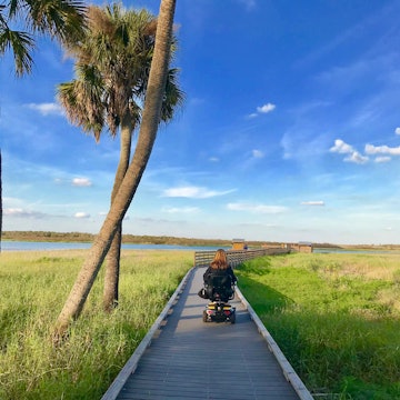 wheelchair user rolls down a wooden birdwalk over seagrass in Florida