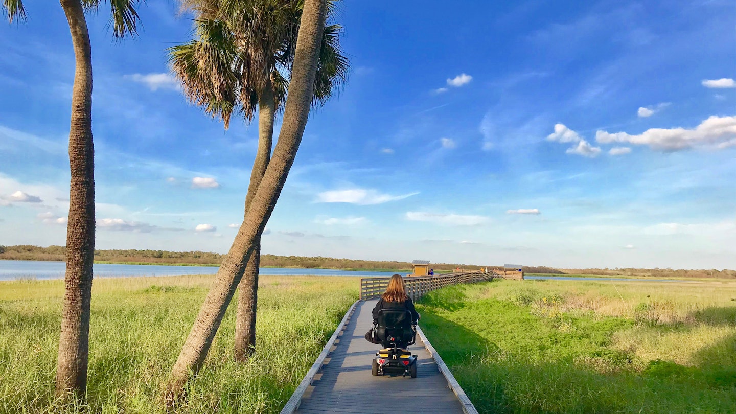 wheelchair user rolls down a wooden birdwalk over seagrass in Florida