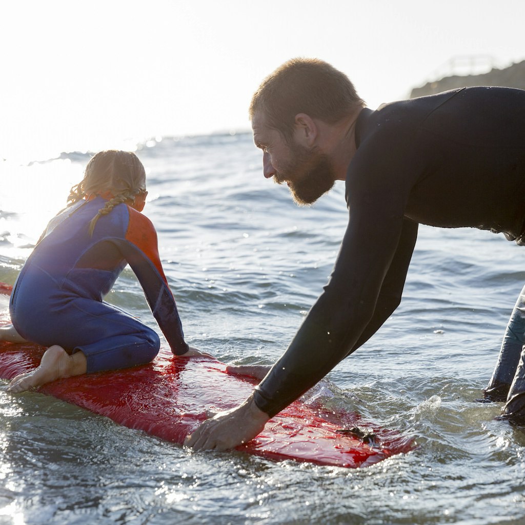 A Father pushes his little daughter into a wave on a surfboard.