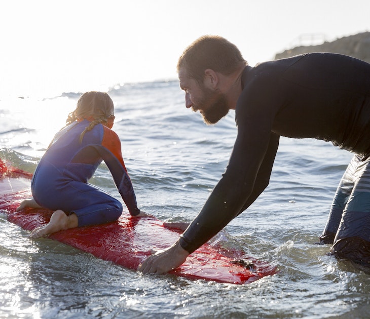 A Father pushes his little daughter into a wave on a surfboard.