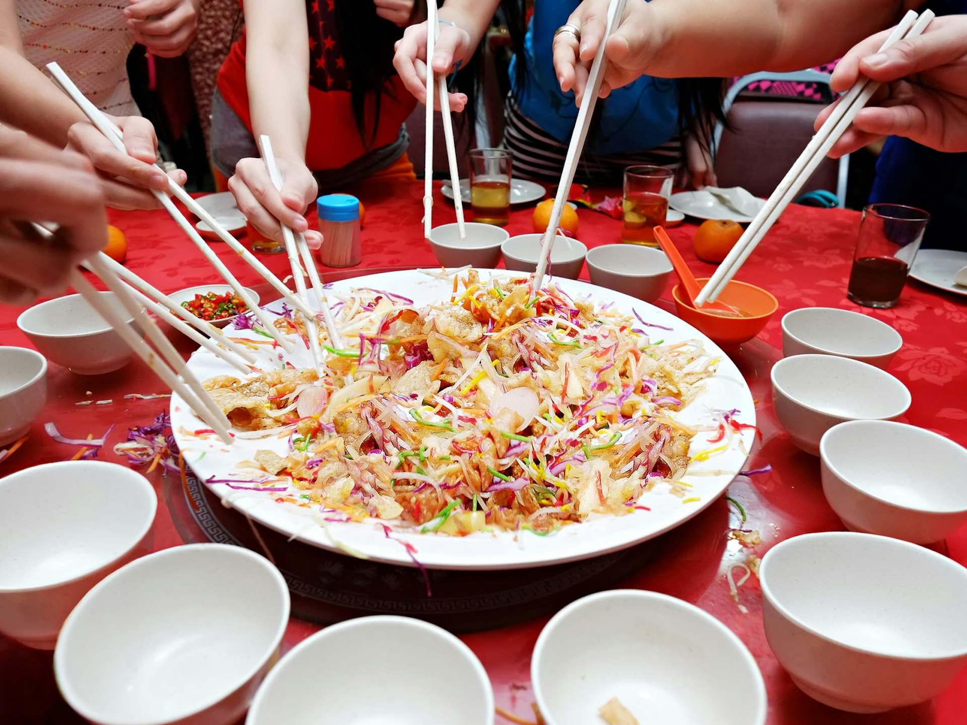 A group of diners pose with their chopsticks over a colourful plate of yee sang: a dish of tossed raw fish that is associated with prosperity for the coming year © Alexlky / Shutterstock