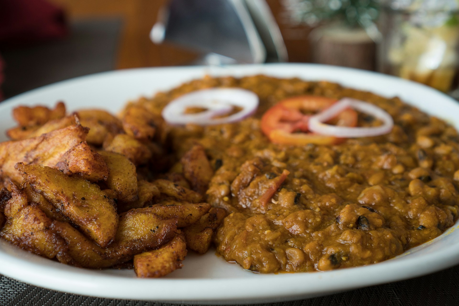 A close-up of the local dish red-red, a combination of fried plantains and stew made from black-eyed beans, palm oil and tomatoes. Atop the stew are some raw rings of onions and a sliced tomato © Elio Stamm / Lonely Planet