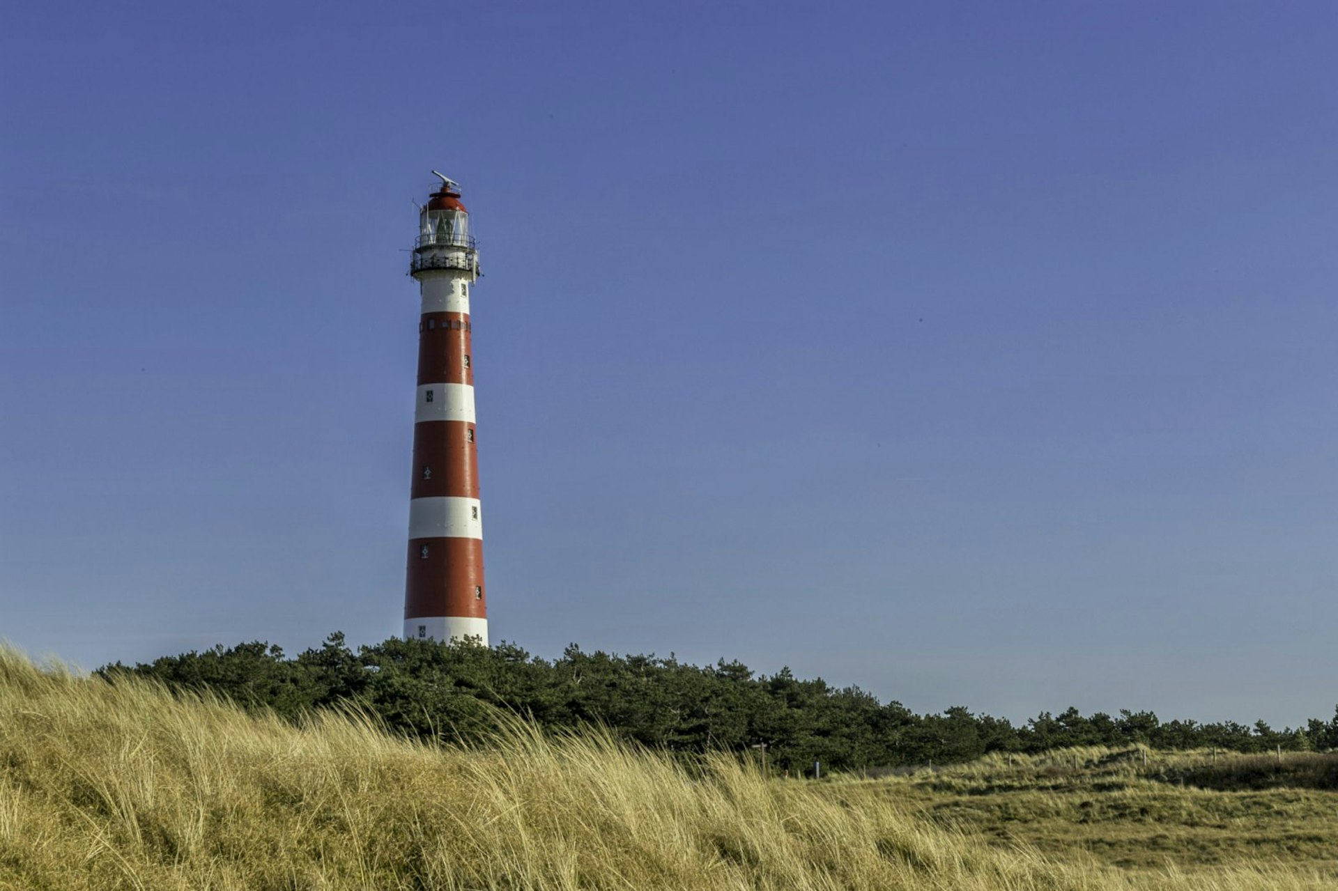 The red and white Ameland Lighthouse in the Netherlands stands against a blue sky
