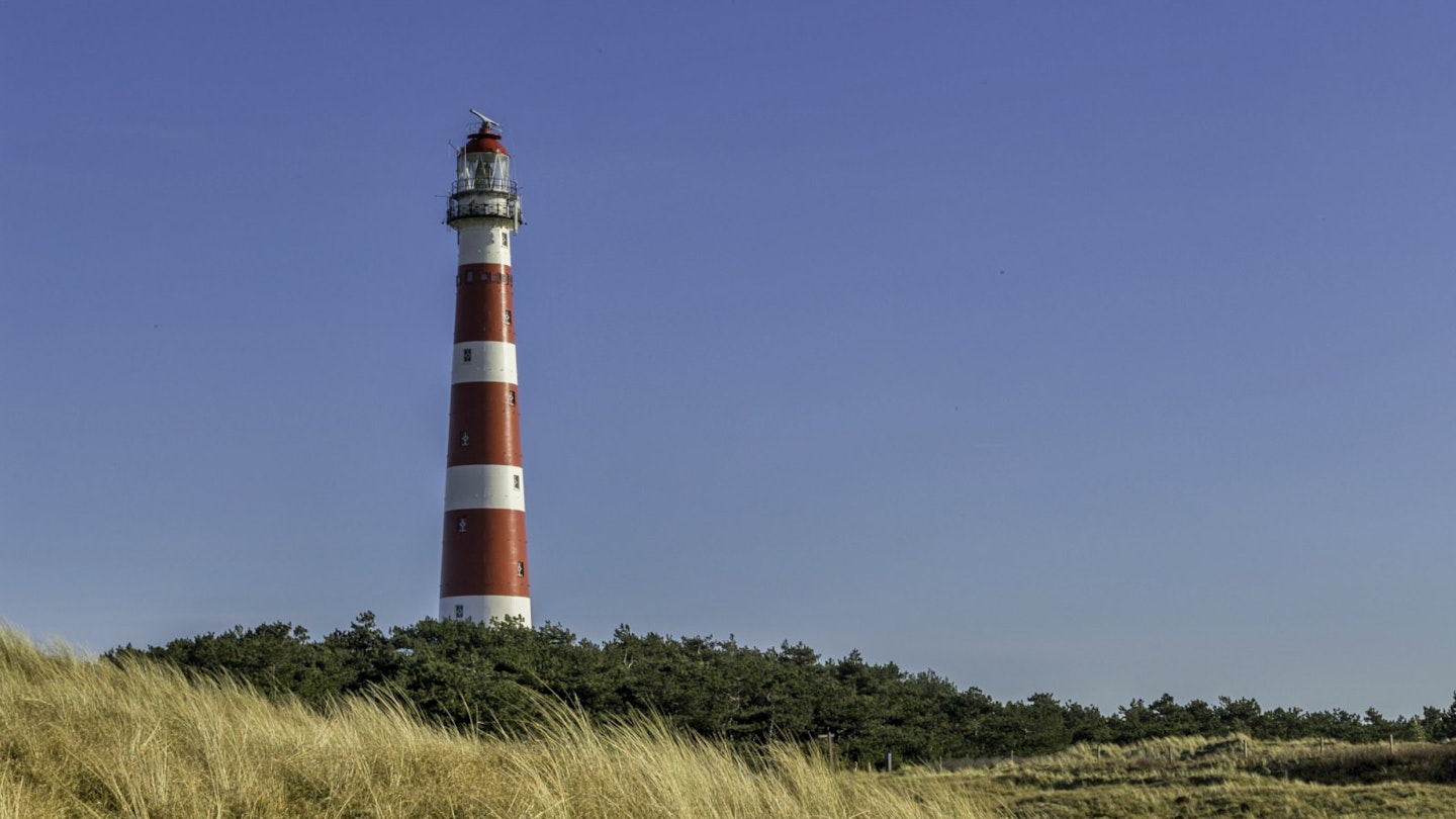 The red and white Ameland Lighthouse in the Netherlands stands against a blue sky