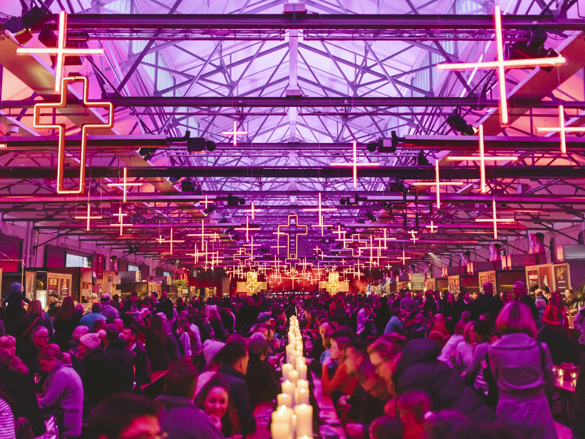 Alternative festivals - crowds gather, seated at long tables, for the winter feast at Dark MOFO in a hall decked in purple light, illuminated crosses and candles