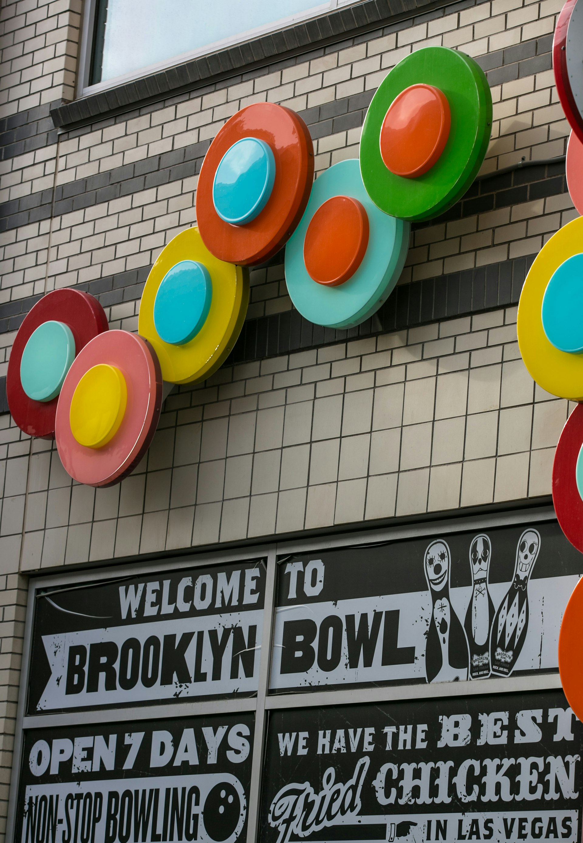 Signage on the outside of Brooklyn Bowl in Las Vegas features white text on a black background, and a random assortment of colored discs that resemble records overhead. © George Rose / Getty Images