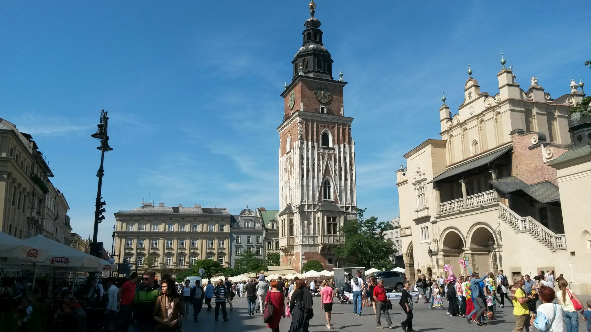 Image of Kraków’s main square showing the Town Hall Tower and Cloth Hall, with crowds of locals and visitors.