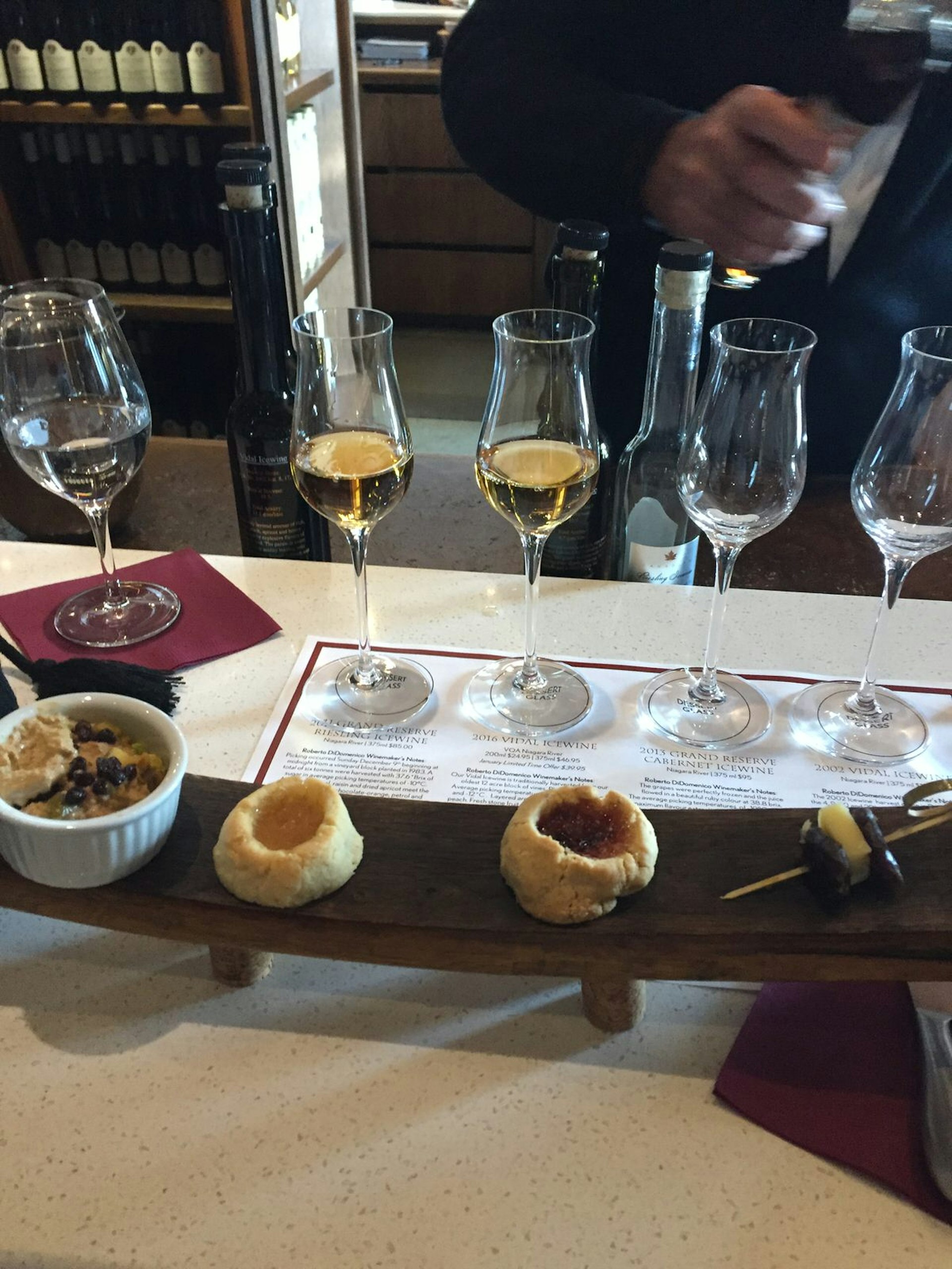 A sommelier pours light-colored ice wines in a row of glasses with a key to the vintage underneath. Various food items are arranged in front of the glasses.