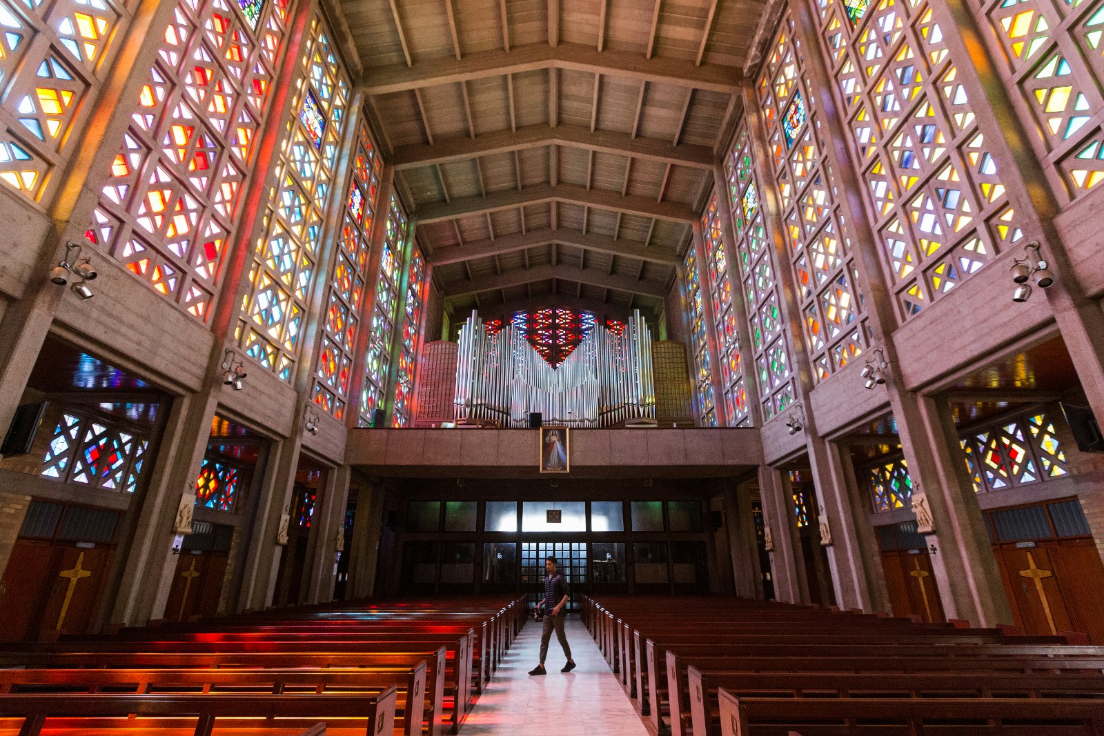Looking down the long aisle of the Cathedral of Christ the King in Hillbrow. The towering vertical walls to the left and right are brilliantly lit stained glass windows, above is a modern vaulted ceiling. © Heather Mason / Lonely Planet