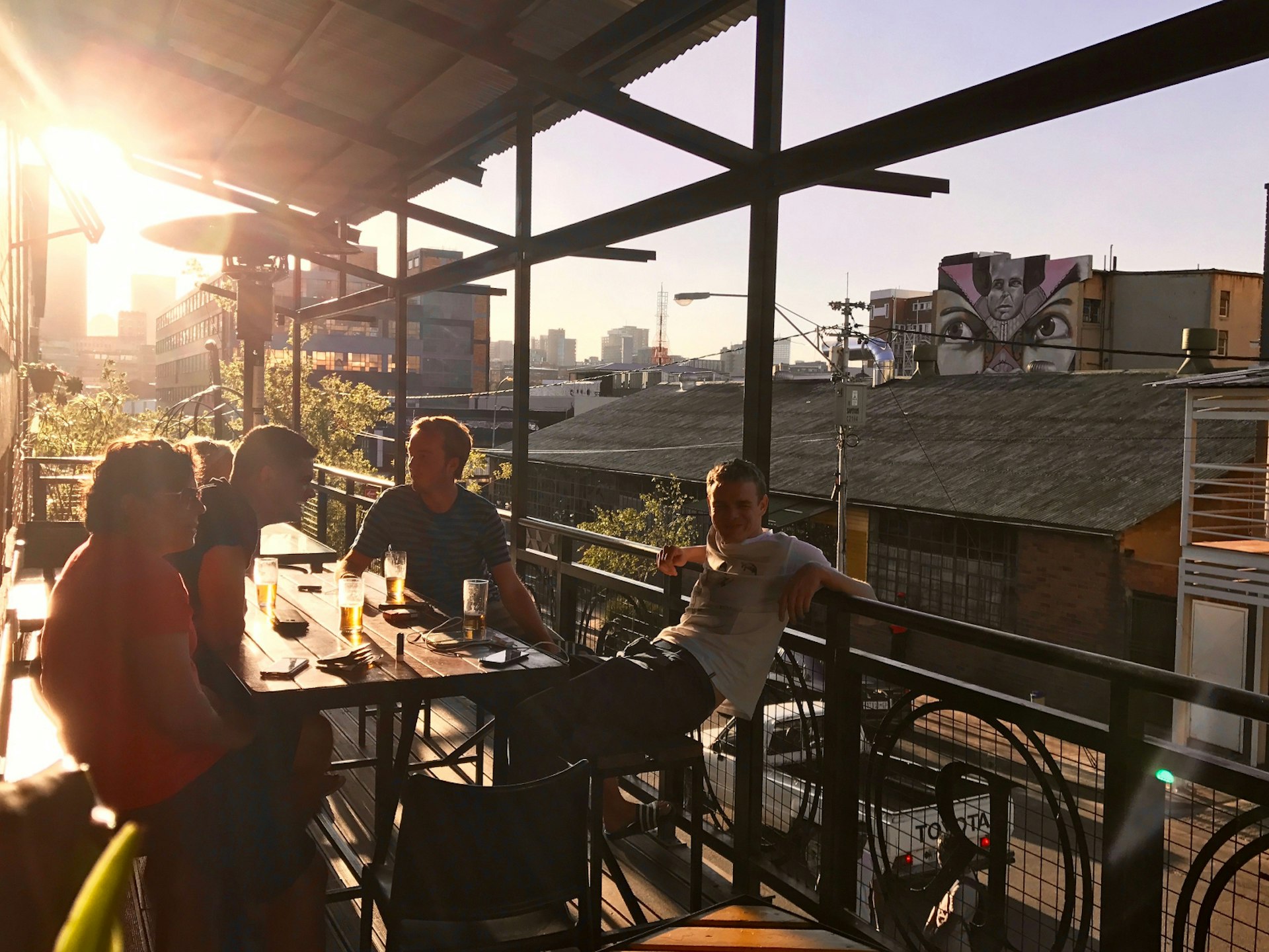 A group of four men enjoy a beer on a covered outdoor balcony on the 1st floor of Curiocity Backpackers. The low sun streams beneath the roof and casts a warm glow © Simon Richmond / Lonely Planet