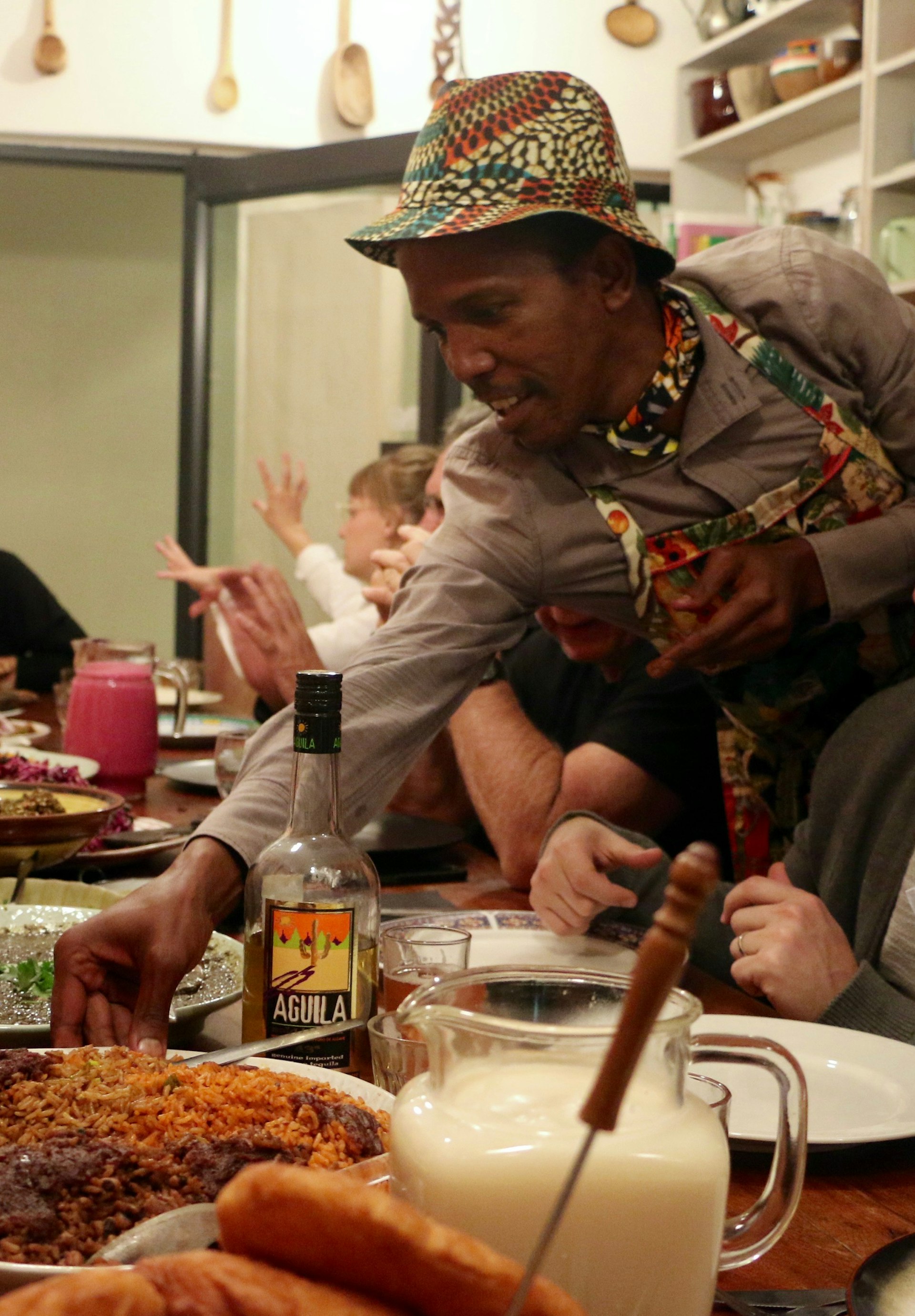 Donning a flamboyant hat and matching apron and scarf, Sanza Sandile places a rich-looking rice dish on the table for his guests at his Yeoville Dinning Club.© Simon Richmond / Lonely Planet