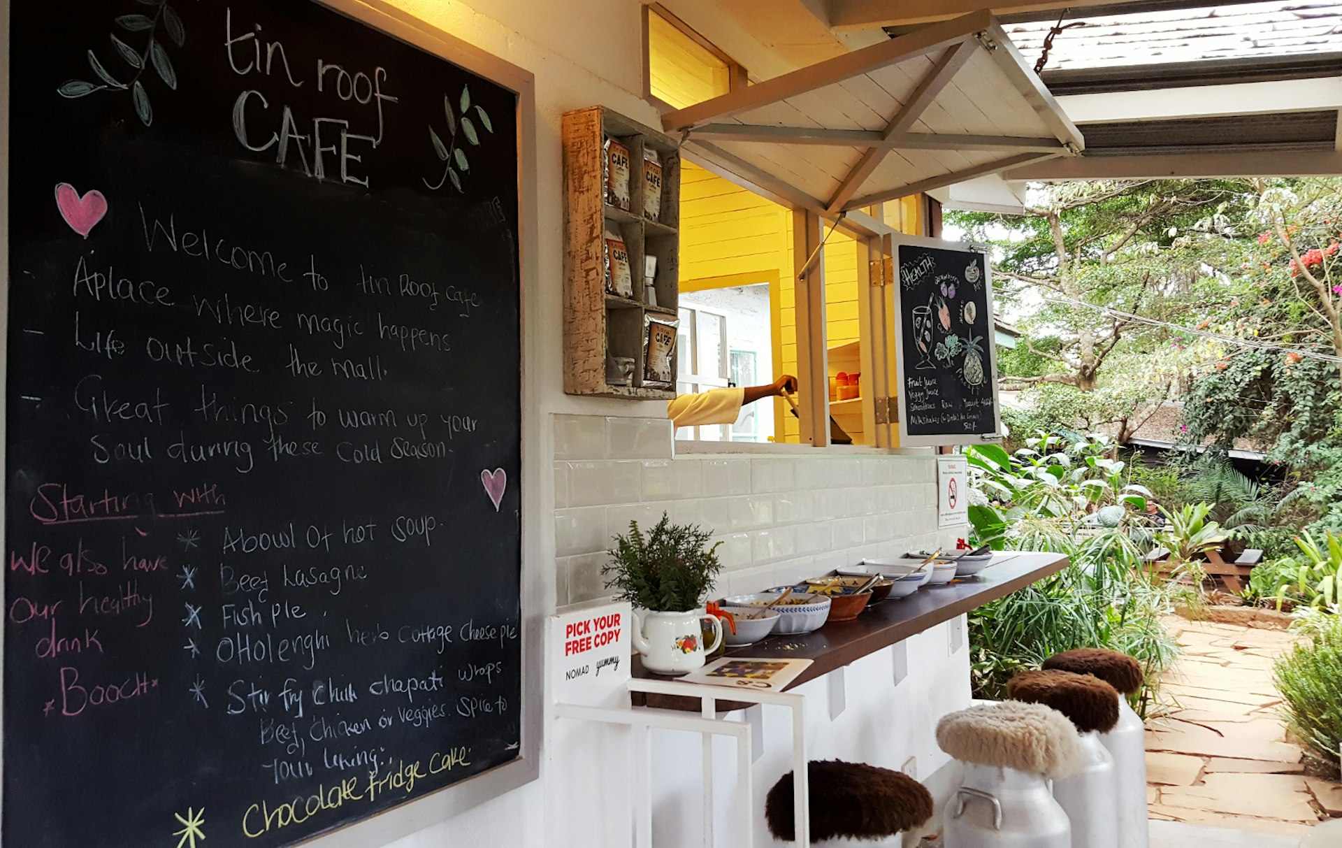 A welcoming open window is set above some bar seating (stools made of industrial milk containers with sheepskin cushions) in the outdoor section of the Tin Roof Cafe, one of Nairobi's 10 best independent cafes © Clementine Logan / Lonely Planet