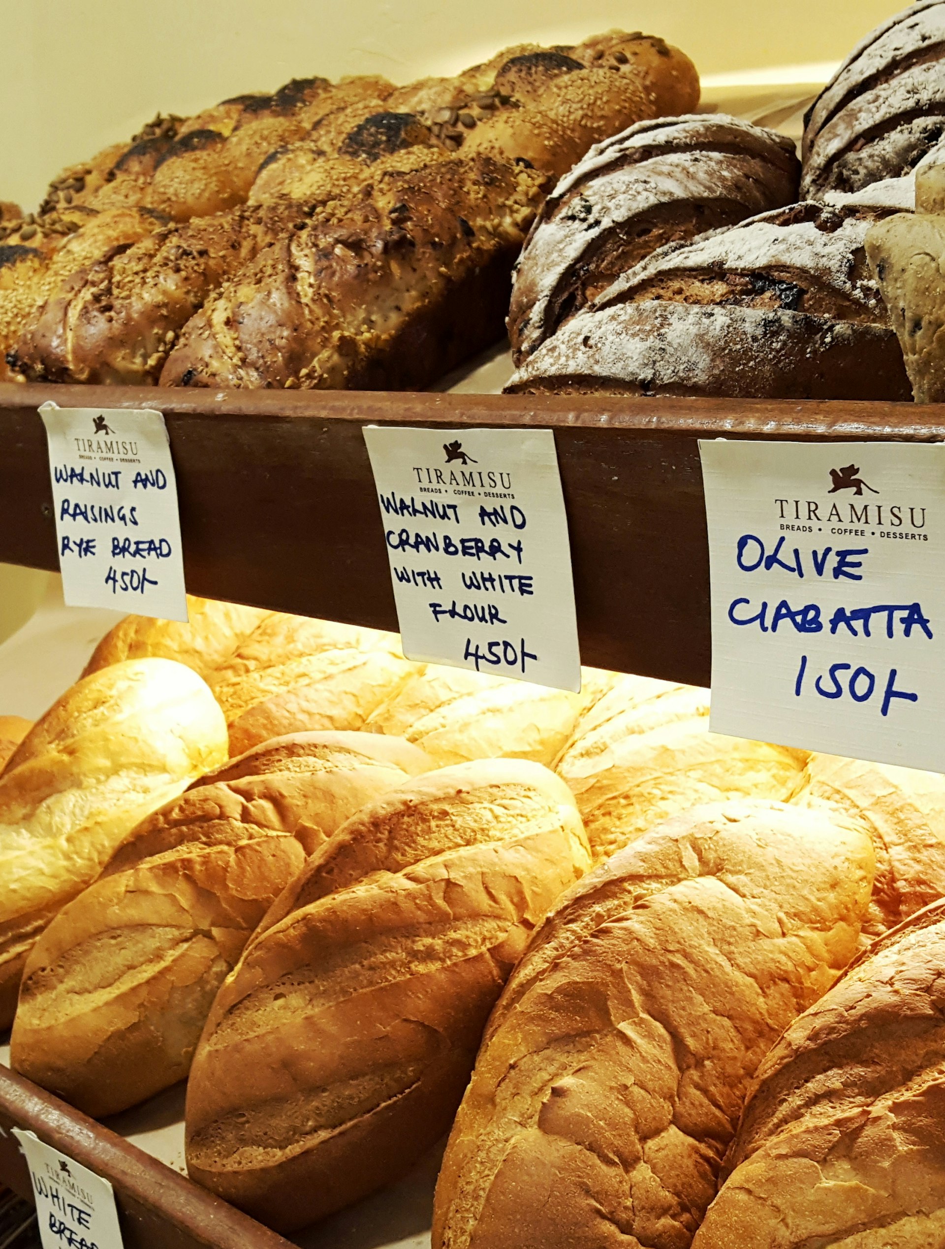 Row upon row of freshly-baked loaves of bread, one dark rye with walnut and raisins, another white bread with walnuts and cranberries, and another olive ciabatta © Clementine Logan / Lonely Planet