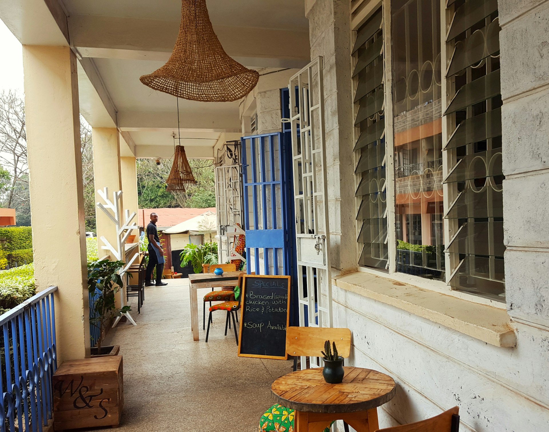An image looking down the verandah of the Wasp and Sprout cafe. Little wooden tables and chairs sit on one side, with wicker lamp shades above. © Clementine Logan / Lonely Planet
