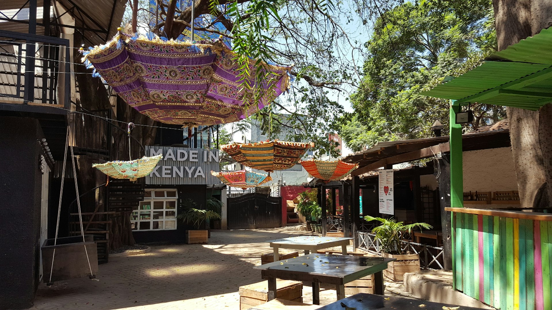 Trees and inverted, colourful Indian umbrellas hanging from branches, shade the outdoor area at the Alchemist bar, which hosts the Made in Kenya shop An open-air sho© Clementine Logan / Lonely Planet