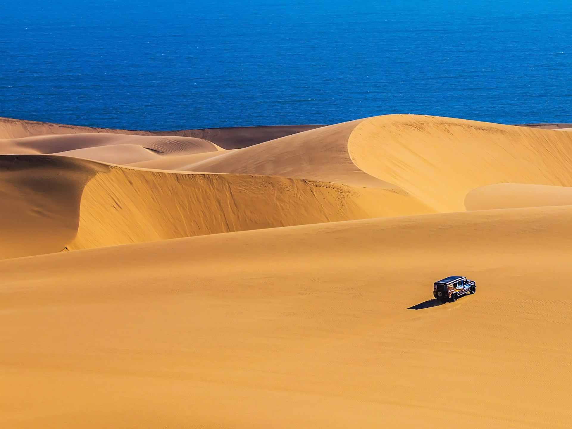 A 4x4 driving towards the coast cover the sand dunes in Sandwich Harbour, Namibia