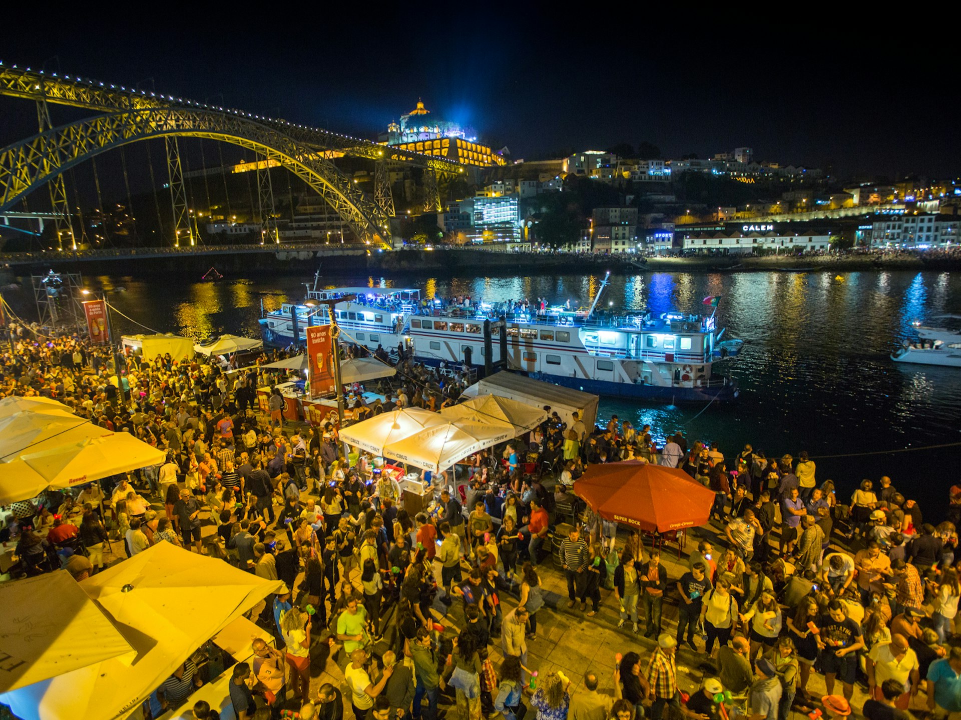 Alternative festivals - the streets of Porto awash with squeaky-hammer-wielding revellers celebrating St John. Crowds mill around market stalls at night, alongside a river with several boats and a huge iron bridge in the background
