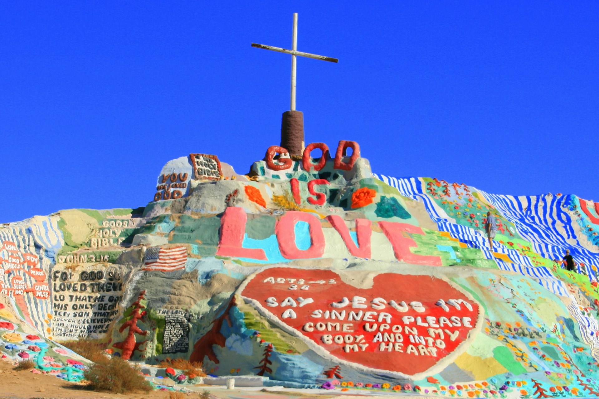 The brightly painted mound of rock and plaster rises with the words God is Love out of the barren desert © Kevin Key / Shutterstock