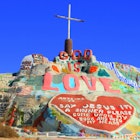 The brightly painted mound of rock and plaster rises with the words God is Love out of the barren desert © Kevin Key / Shutterstock