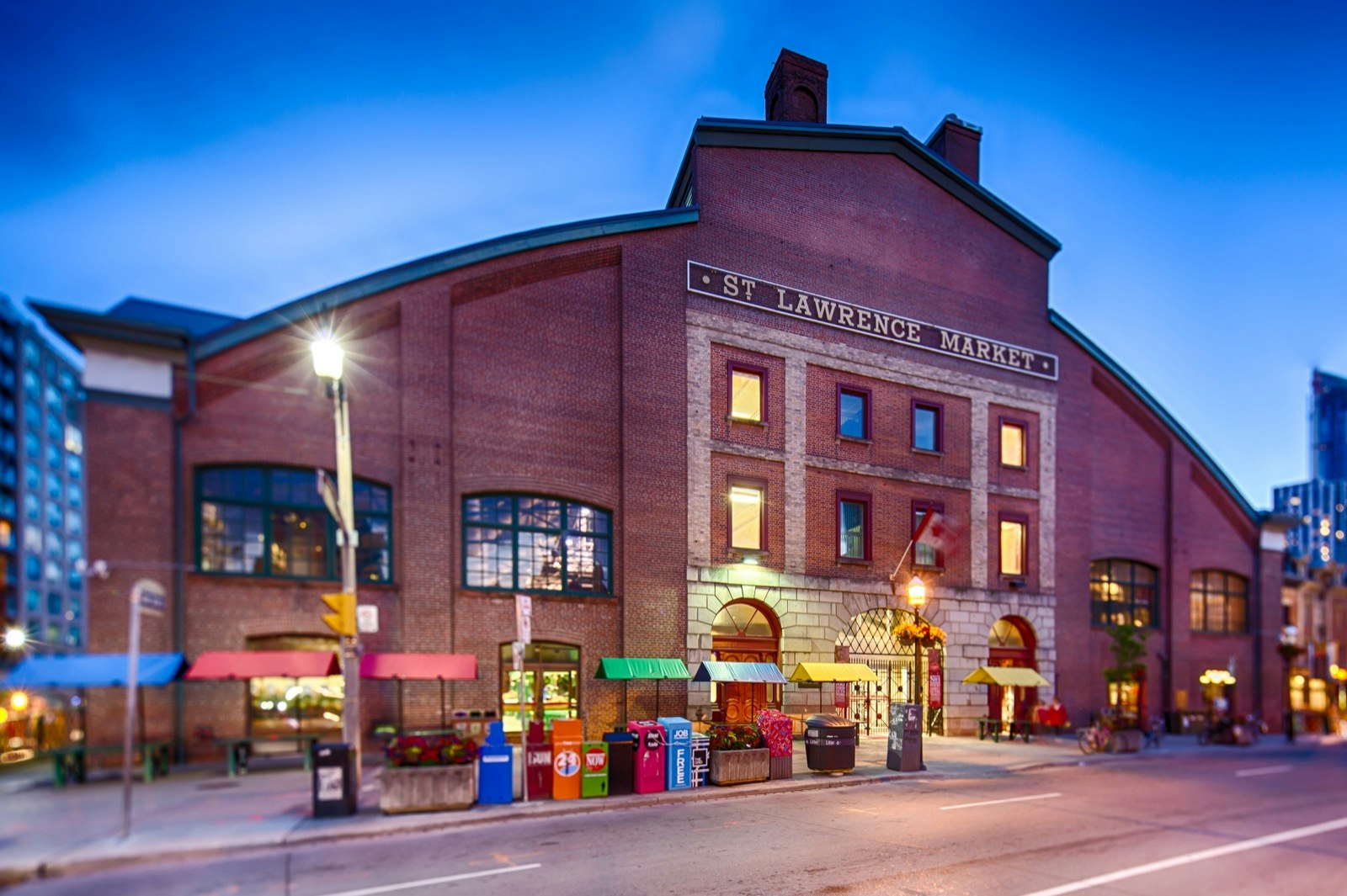 Lights glow at twilight around the giant brick facade of the St. Lawrence Market, one of two major markets in Toronto.