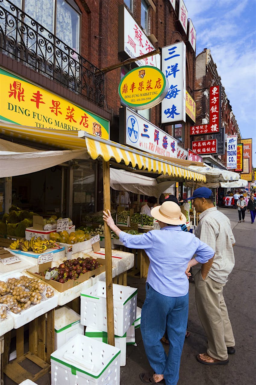 A brightly colored food stand in Toronto, Ontario's chinatown greets two travelers. The signage all uses chinese characters.