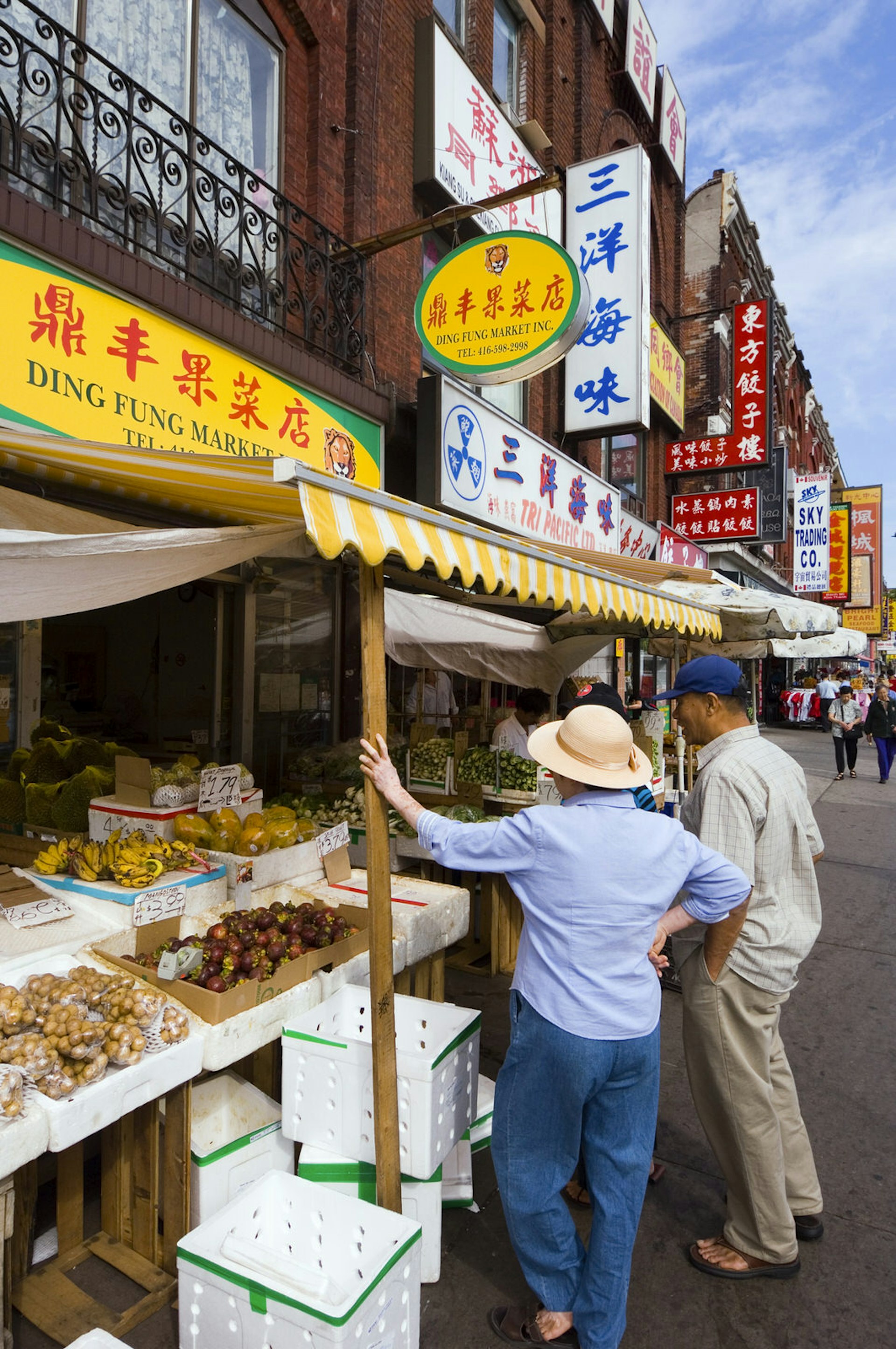 A brightly colored food stand in Toronto, Ontario's chinatown greets two travelers. The signage all uses chinese characters.