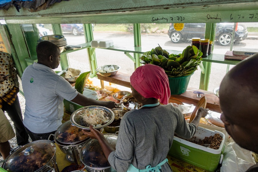 © Within the cramped confines of the pale green food stall are various glass-topped pots and stainless steel bowls filled with ingredients for waakye. Auntie Muni and another man are preparing portions for waiting customers. Outisde its windows you can see automobile traffic in the street. © Elio Stamm / Lonely Planet