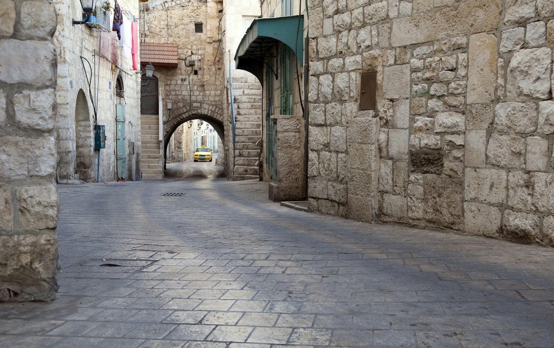 Stone city street and stone buildings on Star Street in the West Bank town of Bethlehem. A Palestinian taxi is in the distance. Image by Joel Carillet / Getty Images
