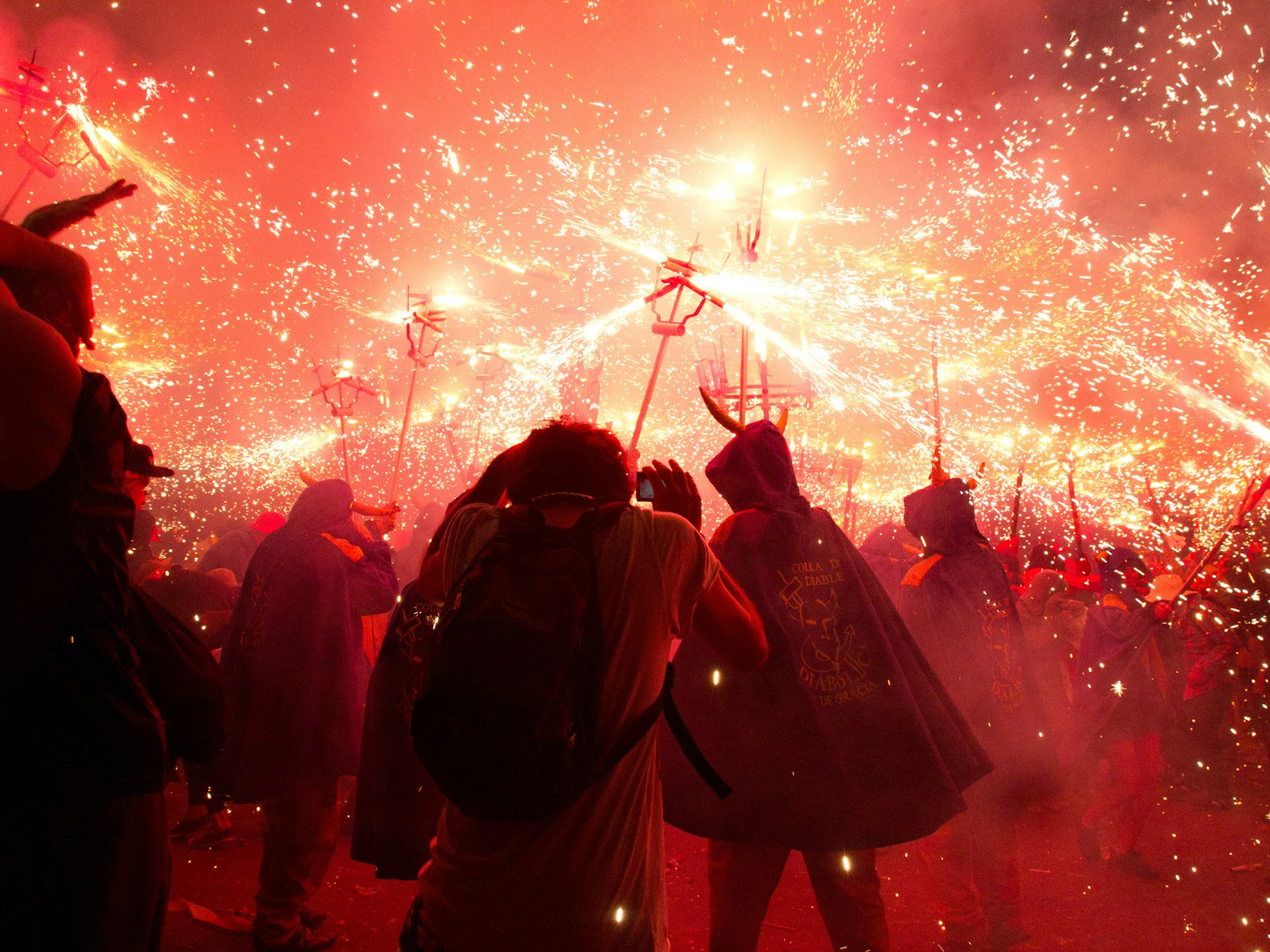 Alternative festivals - people dressed as devils holding fireworks at the end of special sticks. The image is a riot of orange and red sparks with caped and horned figure silhouetted against the light