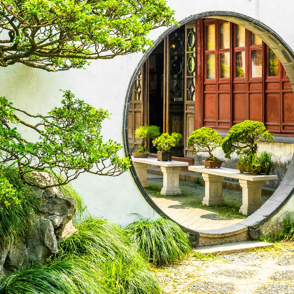 A round moon gate surrounded by white walls and green trees in Suzhou's most famous garden, the Humble Administrator's Garden © Zharov Pavel / Shutterstock